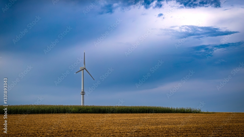 Obraz premium Wind turbine in a field under a blue sky.
