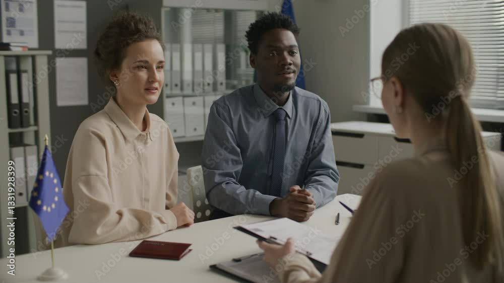Young diverse couple smiling and answering questions from female consular officer while attending immigration interview at European Union embassy Young diverse couple smiling and answering questions from female consular officer while attending immigration interview at European Union embassy