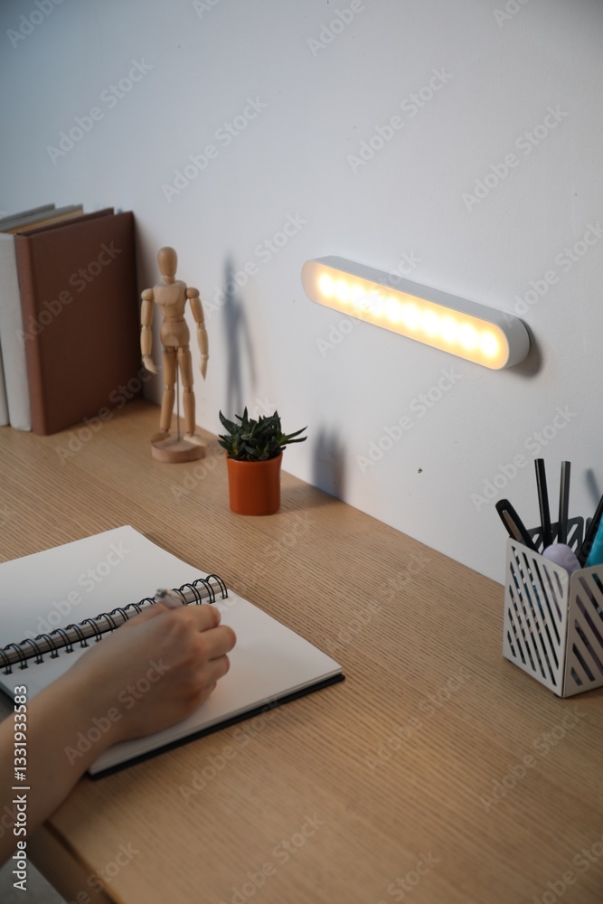 Obraz premium Woman working at desk with LED lamp on wall, closeup