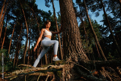 Exploring new places. Woman in fitness clothes is in the forest near the tree