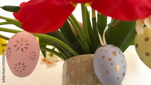 A vase with a bouquet of tulips and daffodils, decorated with colorful eggs, stands on the Easter table. Easter Greeting card