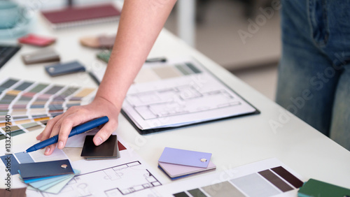 Design Decisions: An interior designer meticulously reviews blueprints, color swatches, and material samples on a workspace, planning the aesthetics of a new project.