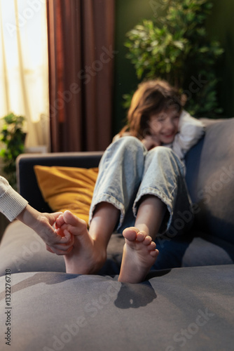 Obraz na plátne Mother tickling daughter's feet on sofa, creating joyful family moment