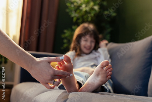 Mother tickling daughter's feet on sofa, having fun at home