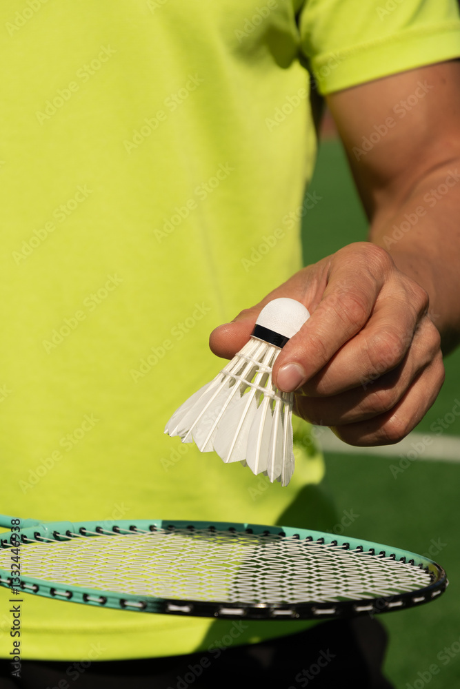 White badminton shuttlecock and badminton rackets in man hands. Summer sports game. Focus on shuttlecock. Outdoor activity. Close up. Vertical.