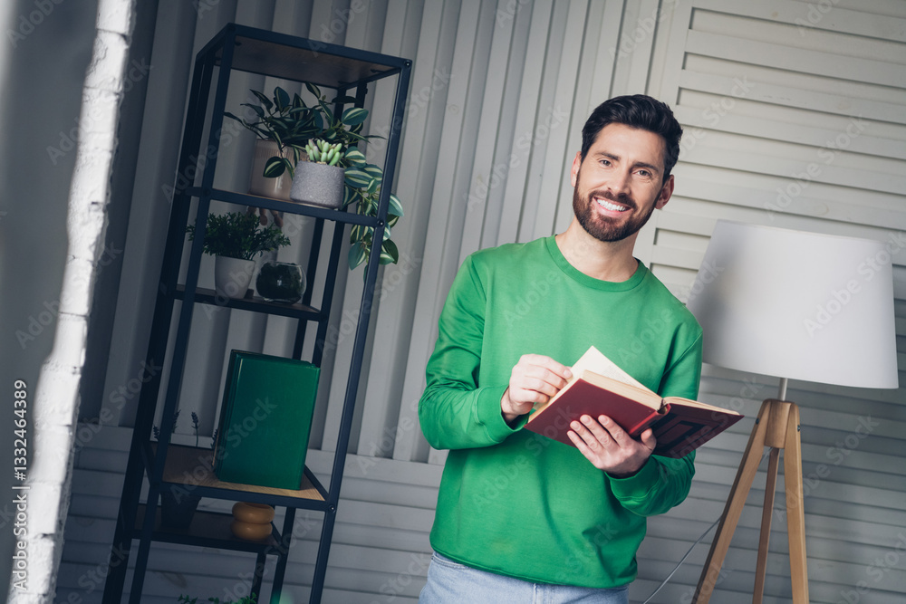 Fototapeta premium Young man in a casual setting reading a book in a cozy, stylish interior with bright lighting