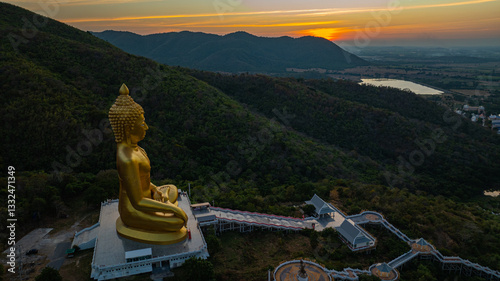 An awe-inspiring view of a big golden Buddha statue atop a hill overlooking a serene valley, captured during the vibrant colors of sunset. aerial view of The biggest golden Buddha at Lopburi Thailand
