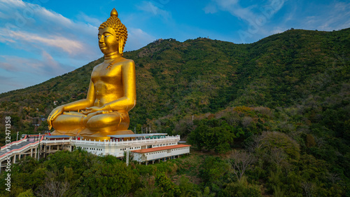 An awe-inspiring view of a big golden Buddha statue atop a hill overlooking a serene valley, captured during the vibrant colors of sunset. aerial view of The biggest golden Buddha at Lopburi Thailand