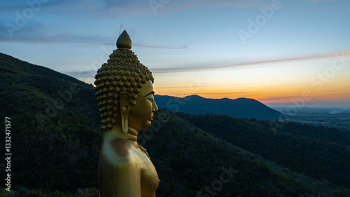 An awe-inspiring view of a big golden Buddha statue atop a hill overlooking a serene valley, captured during the vibrant colors of sunset. aerial view of The biggest golden Buddha at Lopburi Thailand