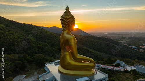 An awe-inspiring view of a big golden Buddha statue atop a hill overlooking a serene valley, captured during the vibrant colors of sunset. aerial view of The biggest golden Buddha at Lopburi Thailand