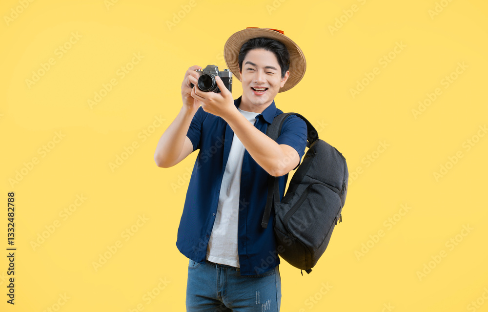 Obraz premium Portrait of young asian man wearing backpack and using camera posing on yellow background