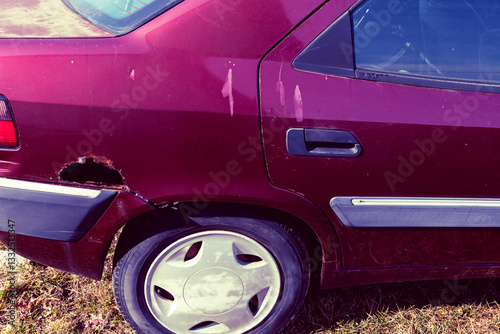 CLOSE UP: natural light. red car. abandoned vintage car abandoned on the road. rust on the fender. decomposing in the countryside. The destroyed car pollutes the environment. photo