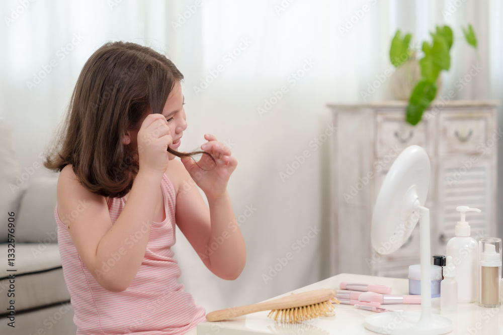 Caucasian young girl sitting at white table examining brown hair strand while looking into mirror. Beauty products and hairbrush arranged neatly on table in bright home interior. Caucasian young girl sitting at white table examining brown hair strand while looking into mirror. Beauty products and hairbrush arranged neatly on table in bright home interior.
