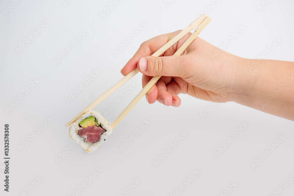 Close-up of a hand using chopsticks to hold a fresh sushi California roll with tuna, avocado, and sesame seeds against a clean white background. Minimalist and appetizing. Close-up of a hand using chopsticks to hold a fresh sushi California roll with tuna, avocado, and sesame seeds against a clean white background. Minimalist and appetizing.