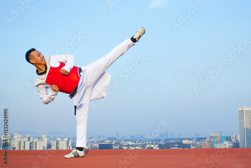 Black belt Taekwondo Player, wearing red chest protection kicking on top of a building