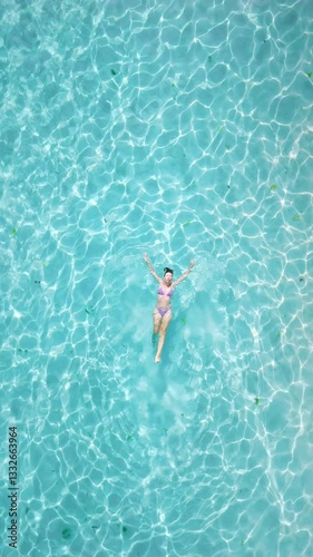 Woman swims in tropical clear sea. Drone view with woman in bikini on vacation, vertical screen