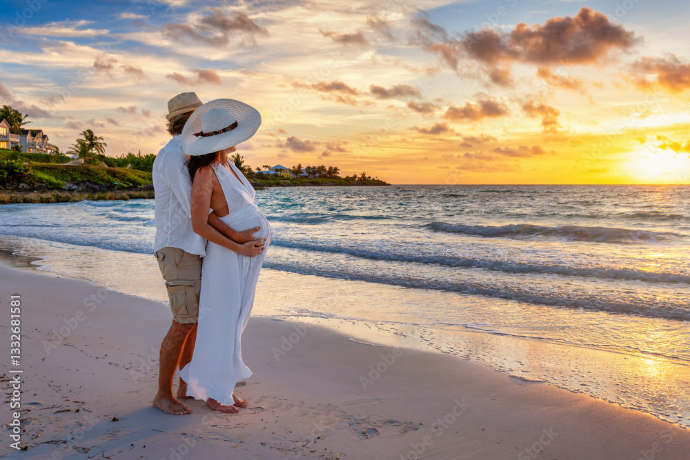 A elegant husband hugging and holding the belly of his pregnant wife on a tropical beach during sunrise time