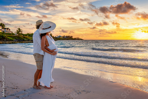 Obraz na płótnie A elegant husband hugging and holding the belly of his pregnant wife on a tropical beach during sunrise time w salonie