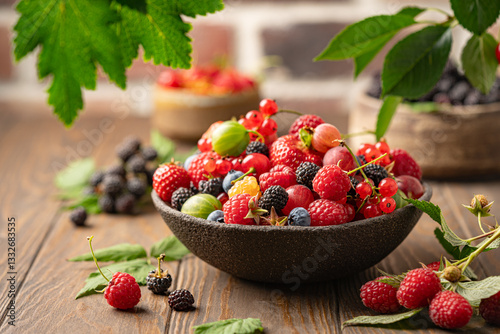 Various fresh berries in a bowl. Mix of different fresh berries on wooden background. Strawberries, raspberries, gooseberries and cherries are presented.
