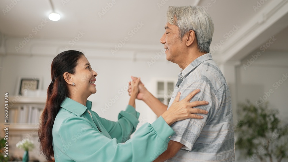 Fototapeta premium Happy grandfather and grandmother with casual cloth holding hand and dancing together at home. Lovely senior couple moving to music and spending time together while supporting at kitchen. Myrmidon.