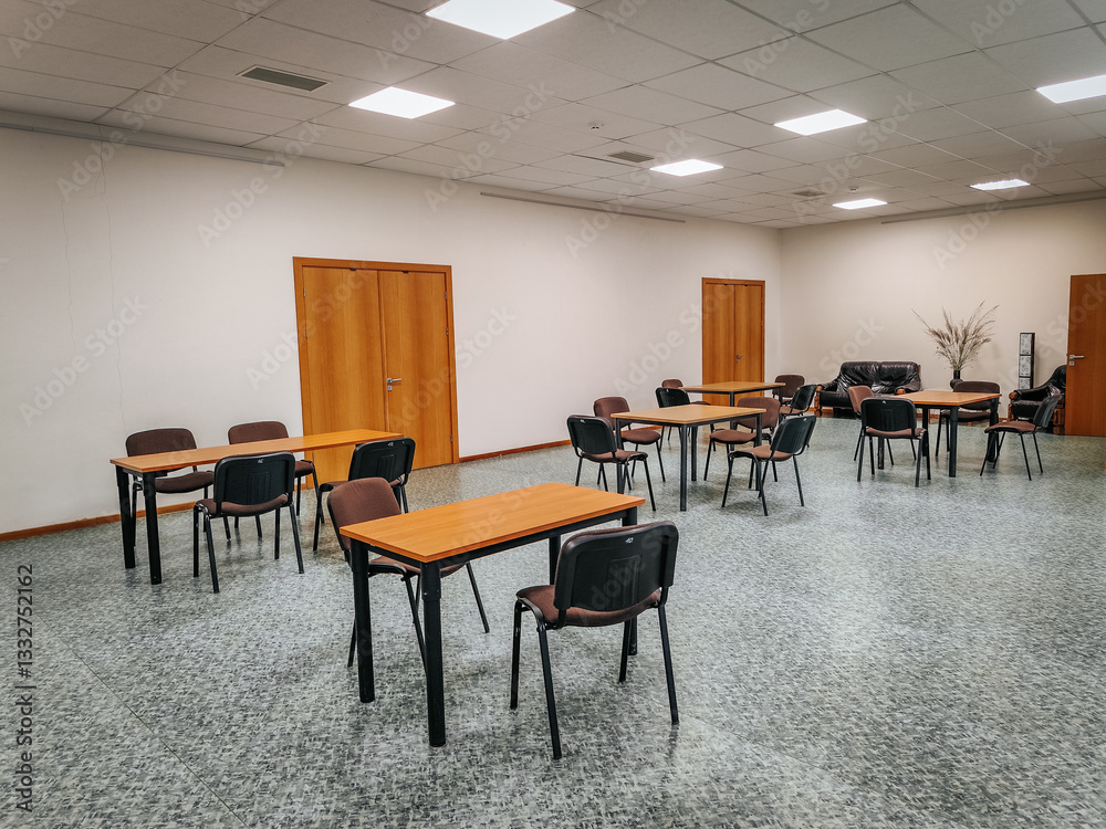 A spacious conference room with wooden tables and black chairs arranged for meetings or events. The minimalist interior features plain walls, wooden doors, and overhead lighting. A spacious conference room with wooden tables and black chairs arranged for meetings or events. The minimalist interior features plain walls, wooden doors, and overhead lighting.