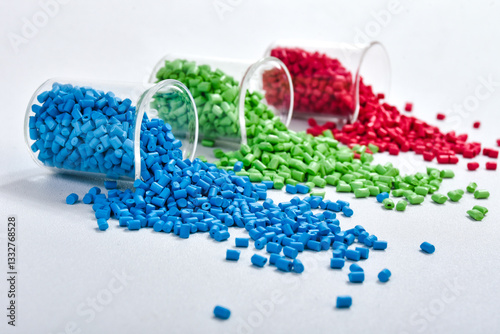 Blue, green and red masterbatch granules spilled from measuring cup, isolated on white background. Color pigment carrier polymer in plastic industry, suitable for plastic company catalog design