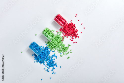 Fotografie Blue, green and red masterbatch granules spilled from measuring cup, isolated on white background