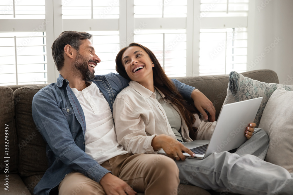 Happy cheerful Latin couple enjoying Internet communication at home, using online TV multimedia service, resting on comfortable home couch with gadget, talking, smiling, laughing Happy cheerful Latin couple enjoying Internet communication at home, using online TV multimedia service, resting on comfortable home couch with gadget, talking, smiling, laughing