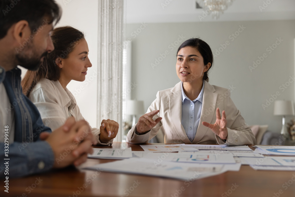 Indian financial broker woman and Caucasian couple of customers discussing investment strategy, planning savings, convenient taxes payment, talking at table with paper analytic diagrams at home Indian financial broker woman and Caucasian couple of customers discussing investment strategy, planning savings, convenient taxes payment, talking at table with paper analytic diagrams at home