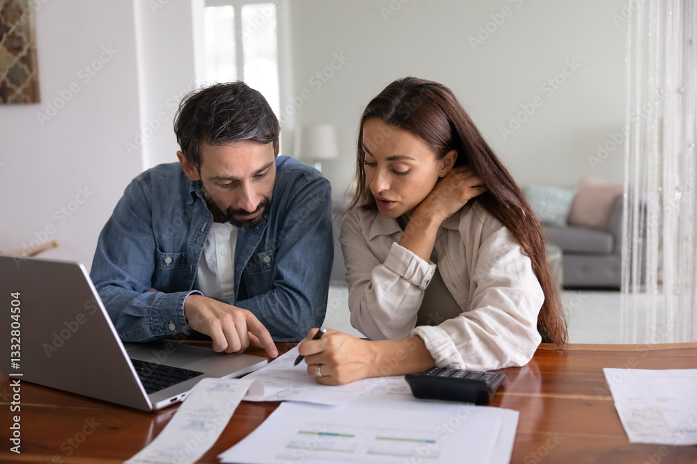Serious young middle aged couple analyzing personal domestic budget at home, checking paper bills, receipts for payment, discussing expenses at table with laptop and calculator Serious young middle aged couple analyzing personal domestic budget at home, checking paper bills, receipts for payment, discussing expenses at table with laptop and calculator