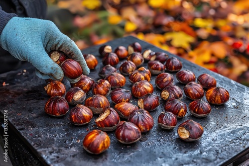 A captivating shot of roasted chestnuts on a metal surface, with a gloved hand selecting one, autumn leaves blurred in the background, seasonal delicacy.