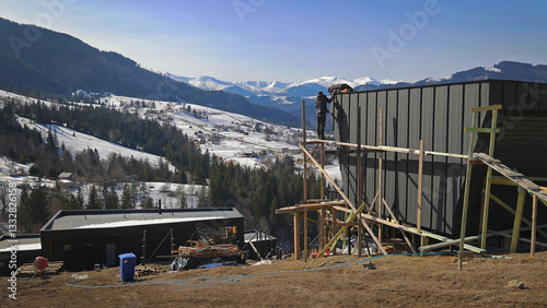 Canvas Print Construction workers building modern house, scenic snowy mountains and forest in background