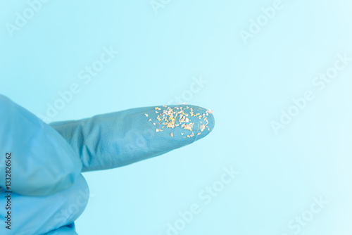 Researcher holding small pieces of Microplastic finger closely with lab glove. On blue background with copy space.