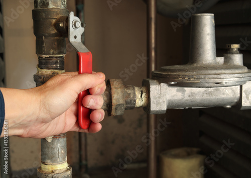 Technician using gas shut-off valve in front of gas pressure regulator. Natural gas boiler supply line for hot water heating. Gas safe, technician or plumbing hot water background. Selective focus.