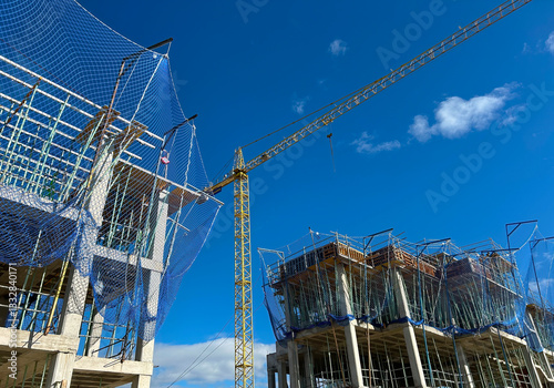 View of the construction site of an apartment building with cranes and safety nets at work, with blue sky and no people working.