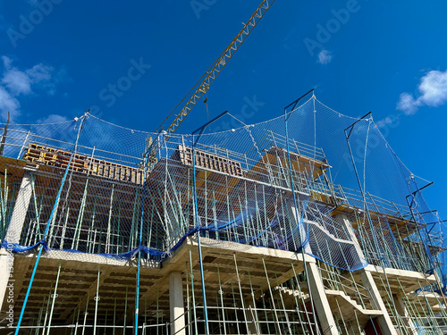 View of the construction site of an apartment building with cranes and safety nets at work, with blue sky and no people working.