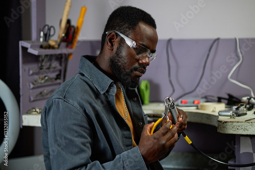 Portrait of African American man in workshop environment wearing safety glasses and using pliers for precision work in industrial setting