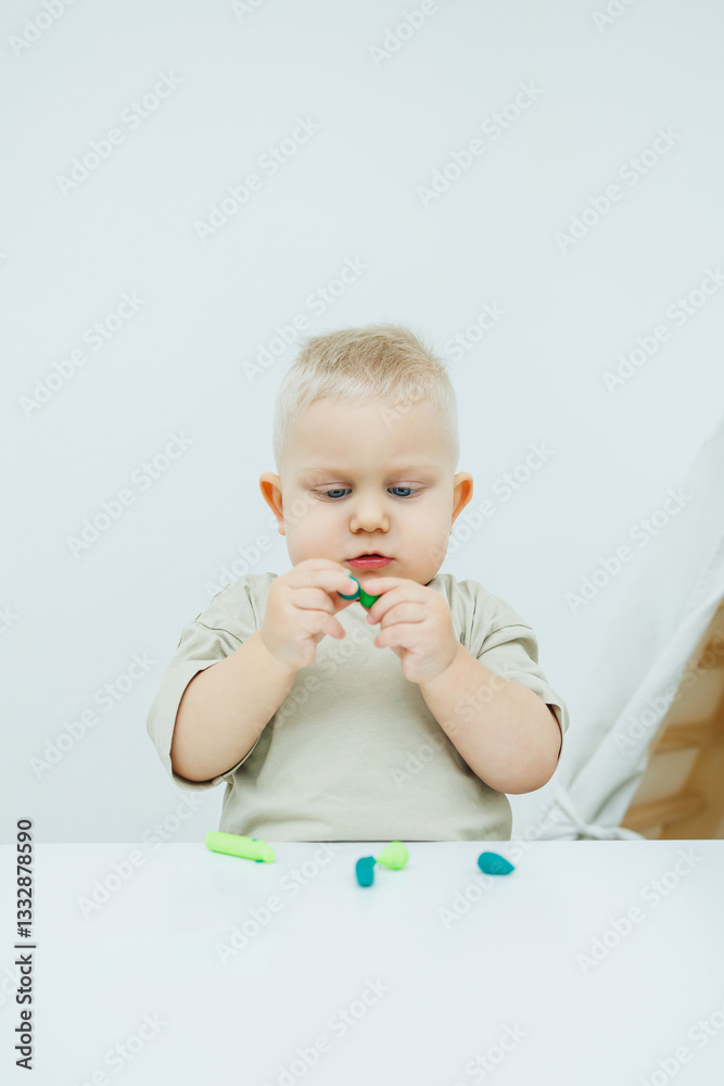 A little one-year-old boy is sculpting plasticine while standing at the table. The child is playing with educational toys. A little one-year-old boy is sculpting plasticine while standing at the table. The child is playing with educational toys.