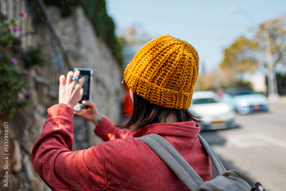 Obraz premium Girl with phone. Young woman taking pictures of flowers on the street. Female hands holding mobile device taking pictures of beautiful plant on sunny day.