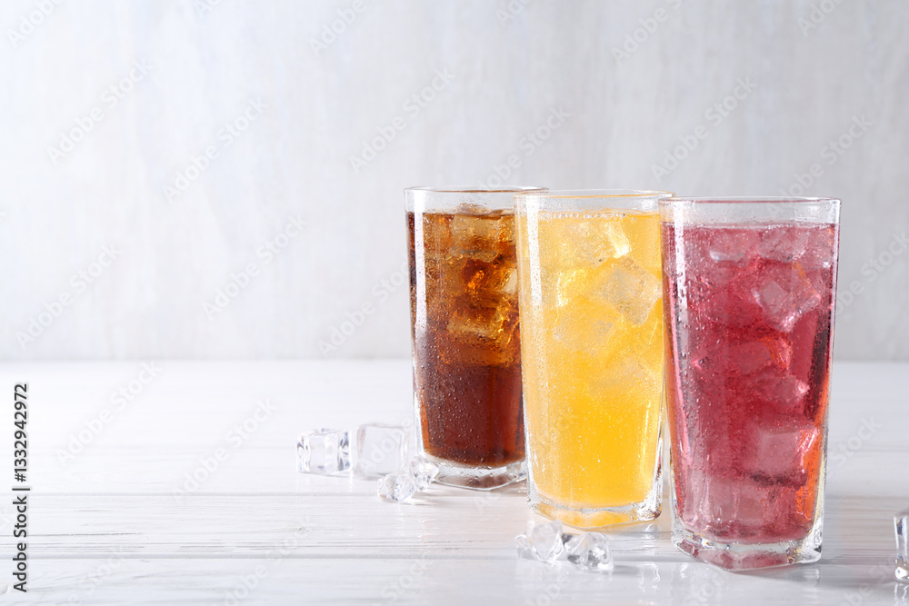 Soda water of different flavors in glasses with ice cubes on white wooden table, space for text Soda water of different flavors in glasses with ice cubes on white wooden table, space for text
