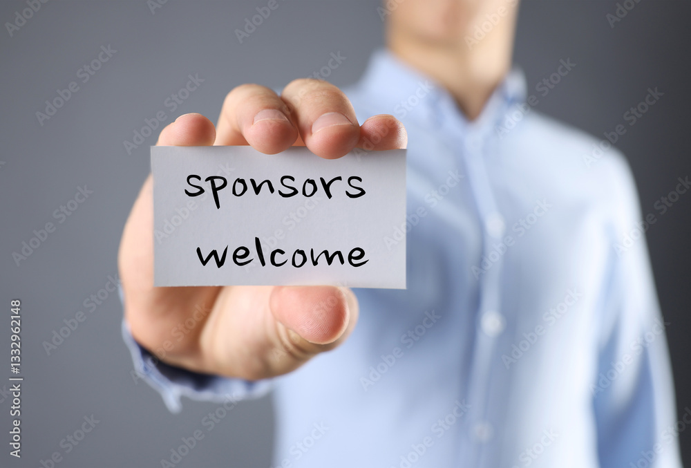Man showing business card with text Sponsors Welcome on grey background, closeup Man showing business card with text Sponsors Welcome on grey background, closeup