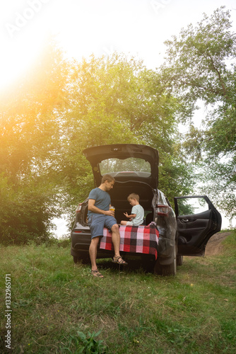 Father and child on outdoor adventure, sitting in car trunk in forest setting. Travel, family weekend, bonding and childhood memories.