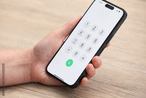 Woman holding smartphone with dialer application at wooden table, closeup
