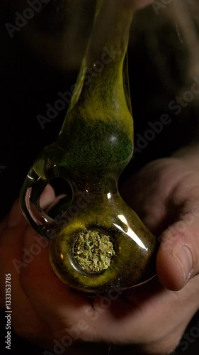 Smoking marijuana from a green glass pipe.  Vertical video of close up recreational drug use, person lights pipe bowl with marijuana and smokes it.