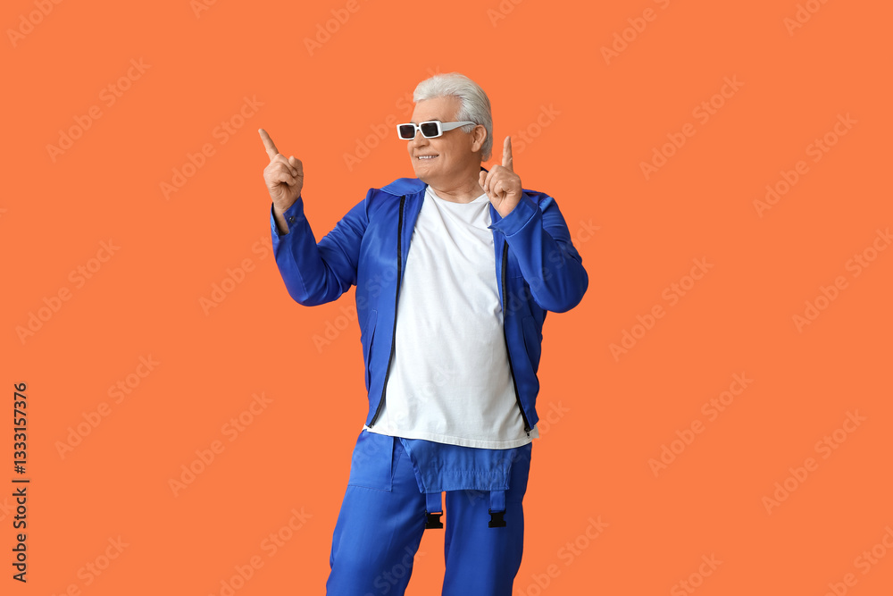 Happy stylish elderly man in sunglasses pointing at something on orange background. National Grandpa Day
