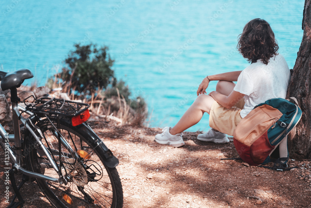 A woman sits with a sea view next to a bicycle. Summer Country Vacation and Adventure Concept