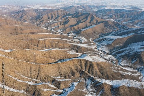 Aerial drone view of winding roads through a Martian-like winter landscape between Garni and Azat Reservoir, Armenia. Dramatic barren hills with snow patches create a surreal travel scenery