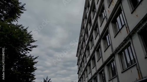A large, aging apartment building with rust stains and cracks on the walls. The overcast sky adds to the feeling of urban decay and abandonment.