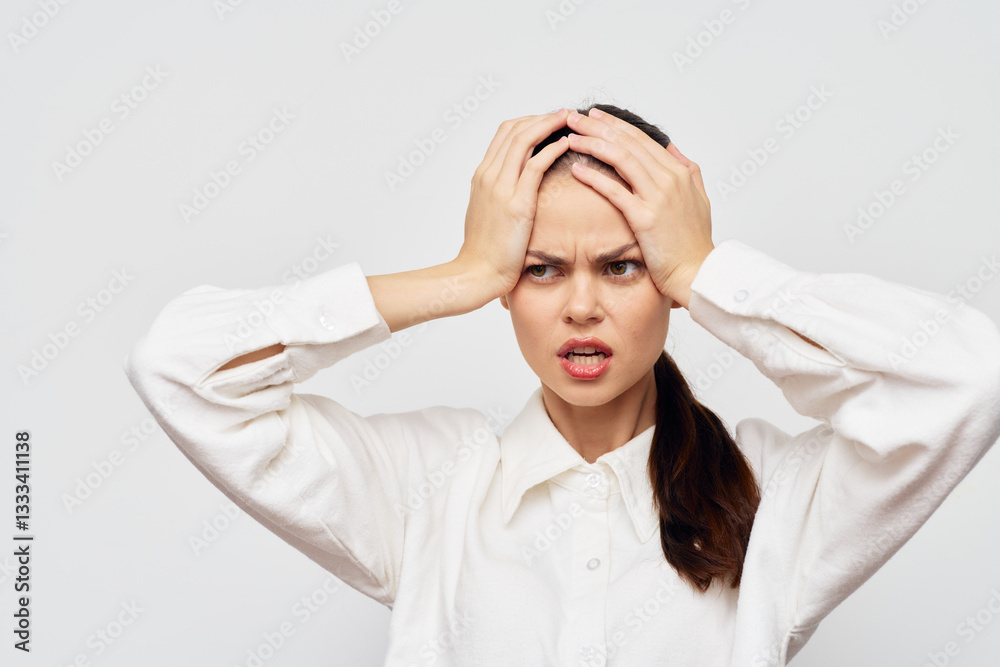 Stress, frustration, young woman with hands on head, expressive face conveying emotions, wearing a white shirt on a light gray background, intense mood, emotional struggle Stress, frustration, young woman with hands on head, expressive face conveying emotions, wearing a white shirt on a light gray background, intense mood, emotional struggle