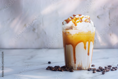 Iced caramel macchiato with whipped cream and caramel drizzle on top on white table.